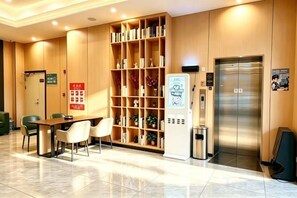 Een hotelhal met een receptiebalie, een zithoek, een boekenkast, een lift en een prullenbak.