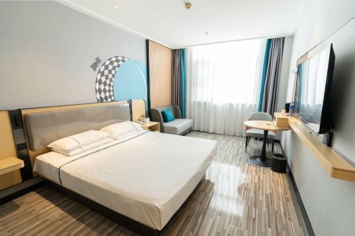 A hotel room with a large bed, a desk, a chair, a TV, and a window with curtains.