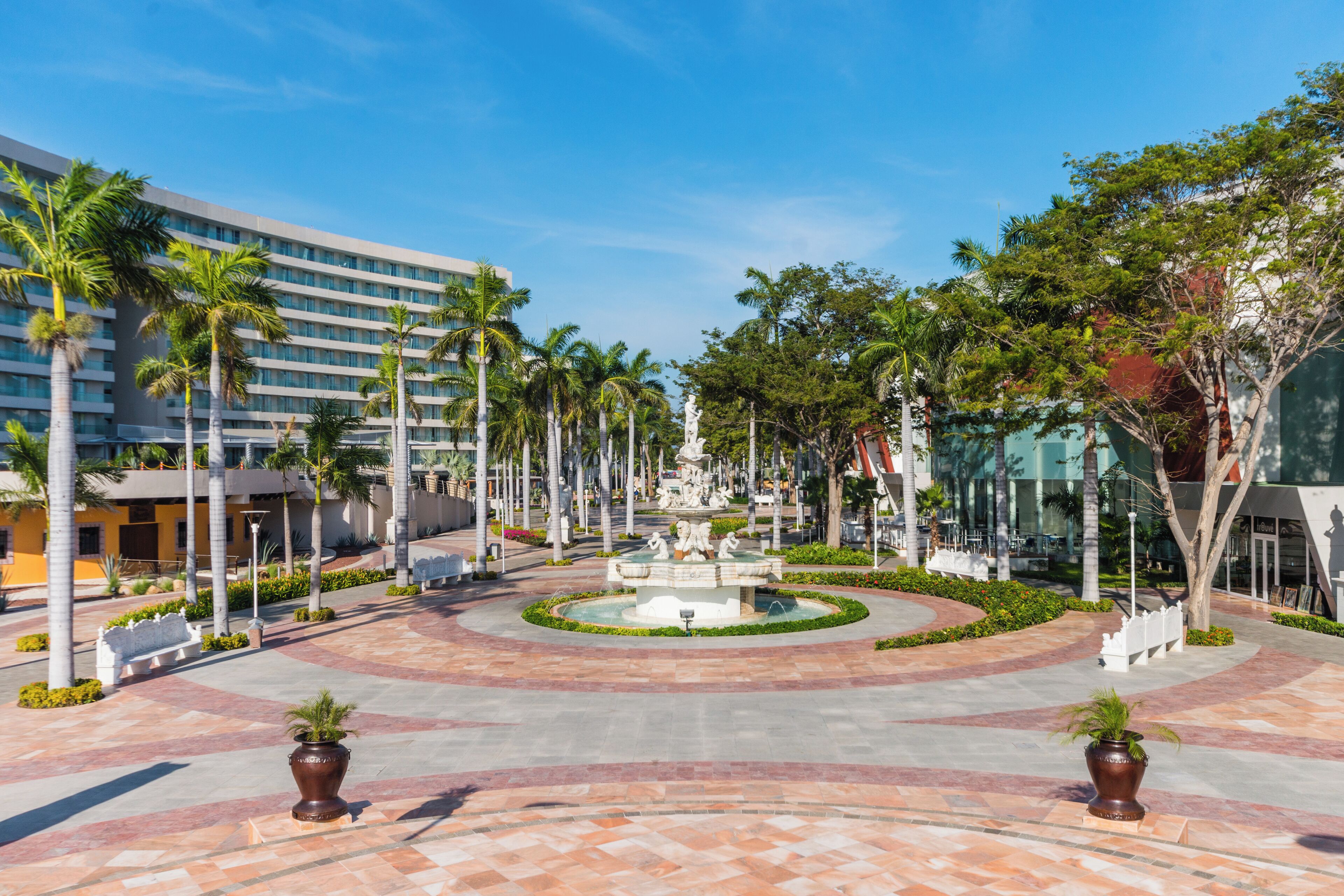 A hotel courtyard with a central fountain, palm trees, and a modern building facade.