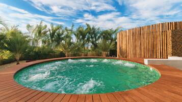 Een houten terras rondom een hottub, met een helderblauwe lucht en palmbomen op de achtergrond.