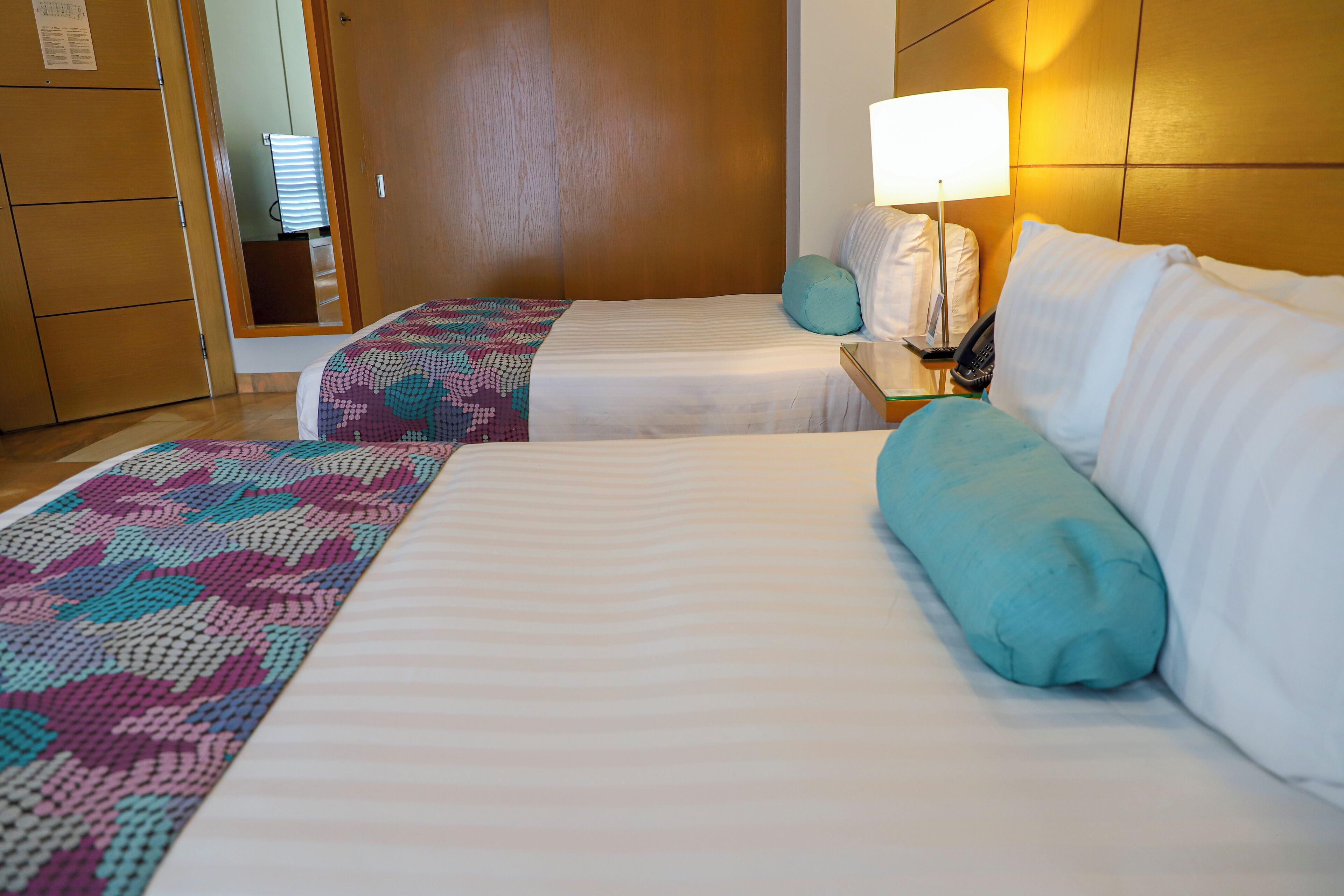 A hotel room with two beds, a nightstand with a lamp, and a wooden wardrobe.
