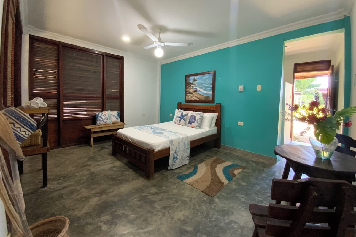 Un dormitorio con cama, escritorio, silla, ventilador de techo y ventana con vistas al exterior.