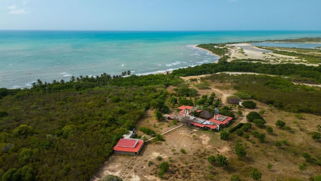 An aerial view of a coastal property with a red-roofed building, a water tower, and a beach in the background.