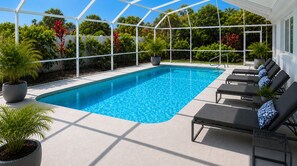 Ein Swimmingpool mit Liegestühlen und Topfpflanzen, umgeben von einem weißen Zaun und viel Grün.