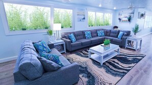 A spacious living room with a grey sectional sofa, a coffee table, and a rug. There are large windows with a view of greenery outside. - Walk to siesta key (Siesta Key)