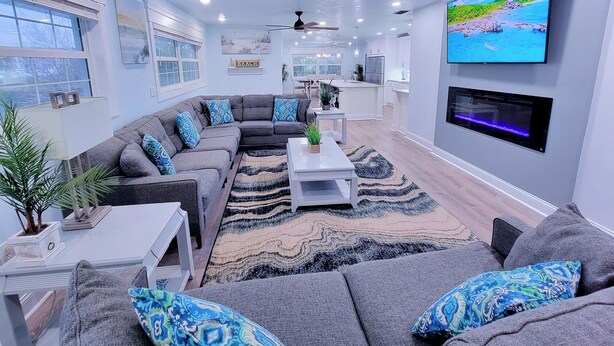 A modern living room with a sectional sofa, a flat-screen TV, ceiling fans, and a kitchen in the background. - Walk to siesta key (Siesta Key)
