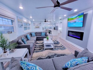 A modern living room with a sectional sofa, a flat-screen TV, ceiling fans, and a kitchen in the background. - Walk to siesta key (Siesta Key)