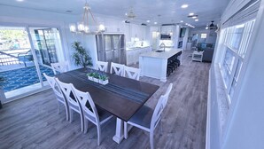A modern kitchen with white cabinetry, a central island with bar stools, and a dining area with a dark table and white chairs. - Walk to siesta key (Siesta Key)