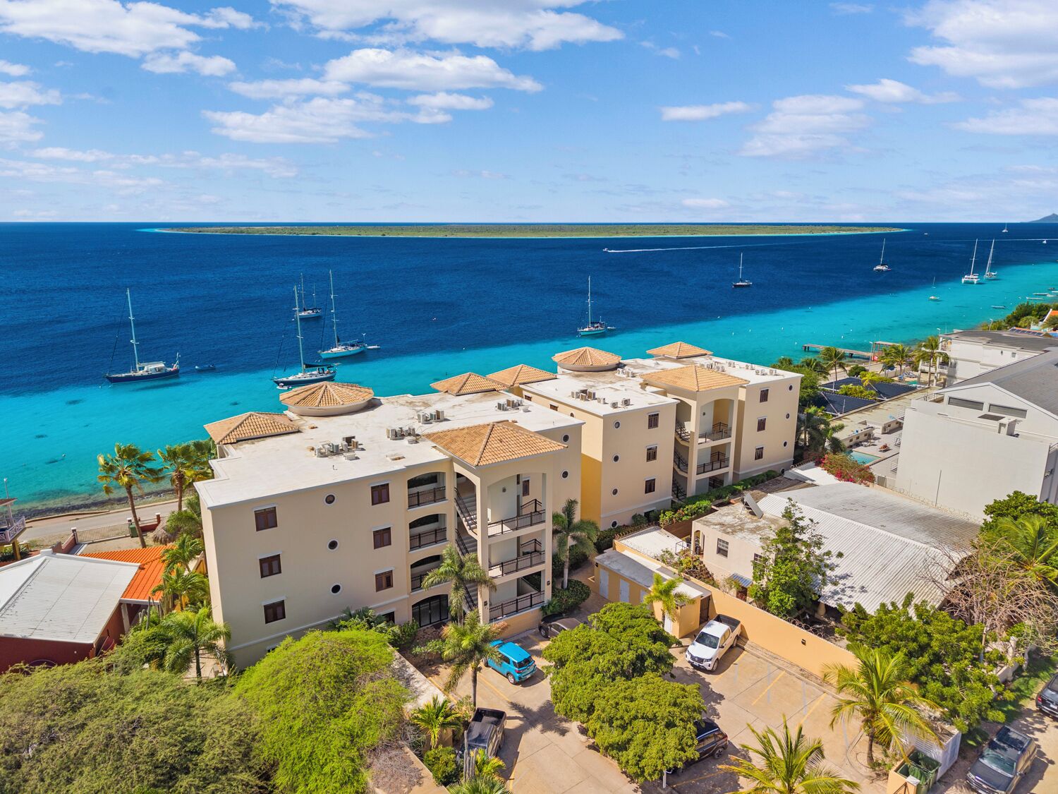 Ein Hotel an der Küste mit mehreren Balkonen, einem Parkplatz und Blick auf das Meer mit Booten.
