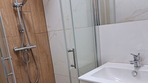 Uma casa de banho moderna com cabine de duche em vidro, uma pia branca e painéis de madeira.