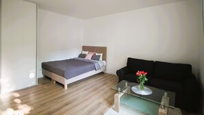 Quarto moderno com cama, sofá preto e mesa de centro de vidro com um vaso de flores.