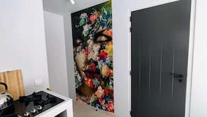 Ein Zimmer mit einer schwarzen Tür, einer weißen Wand und einem farbenfrohen floralen Gemälde an der Wand.