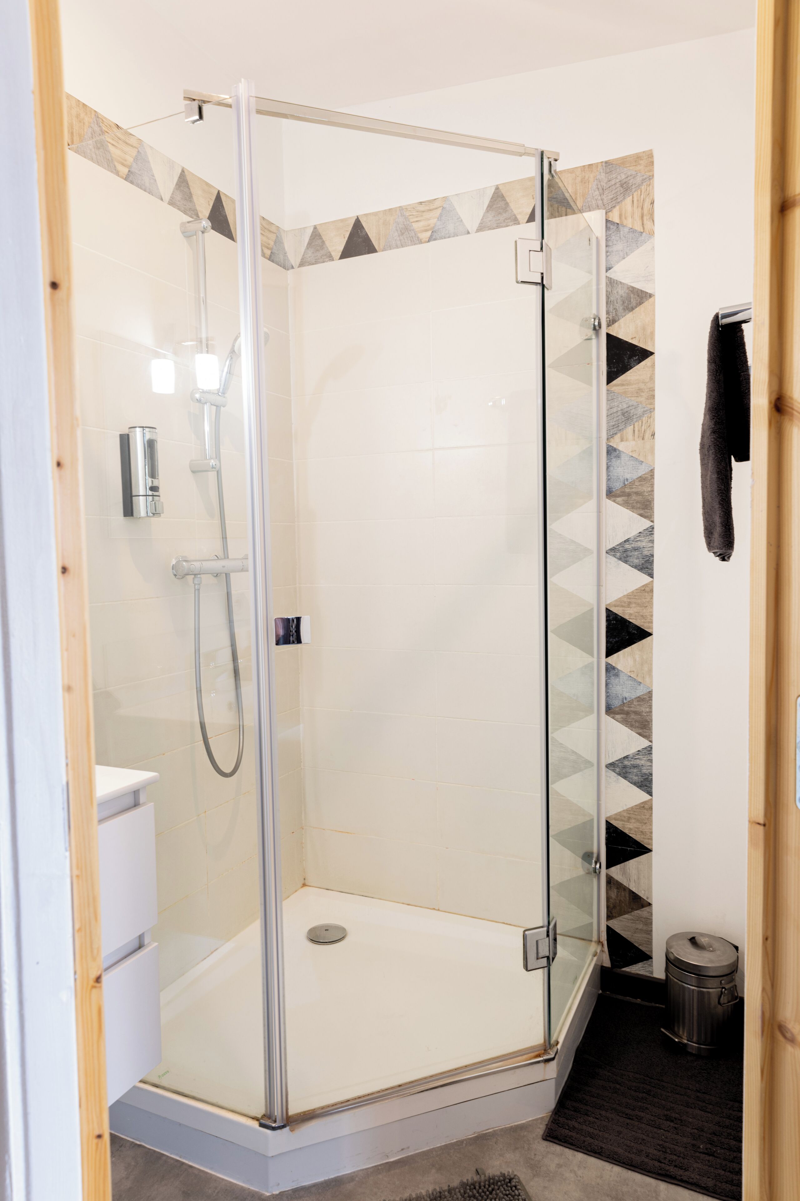 A glass-enclosed shower stall with a white tiled wall and a geometric-patterned accent wall.