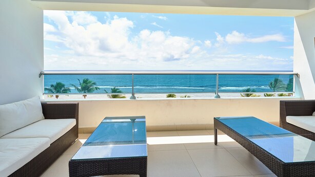 Ein Balkon mit Blick auf das Meer, ausgestattet mit Korbsesseln und einem Tisch mit Glasplatte.