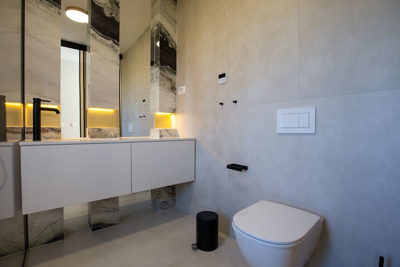 A modern bathroom with a marble vanity, a toilet, and a wall-mounted light fixture.