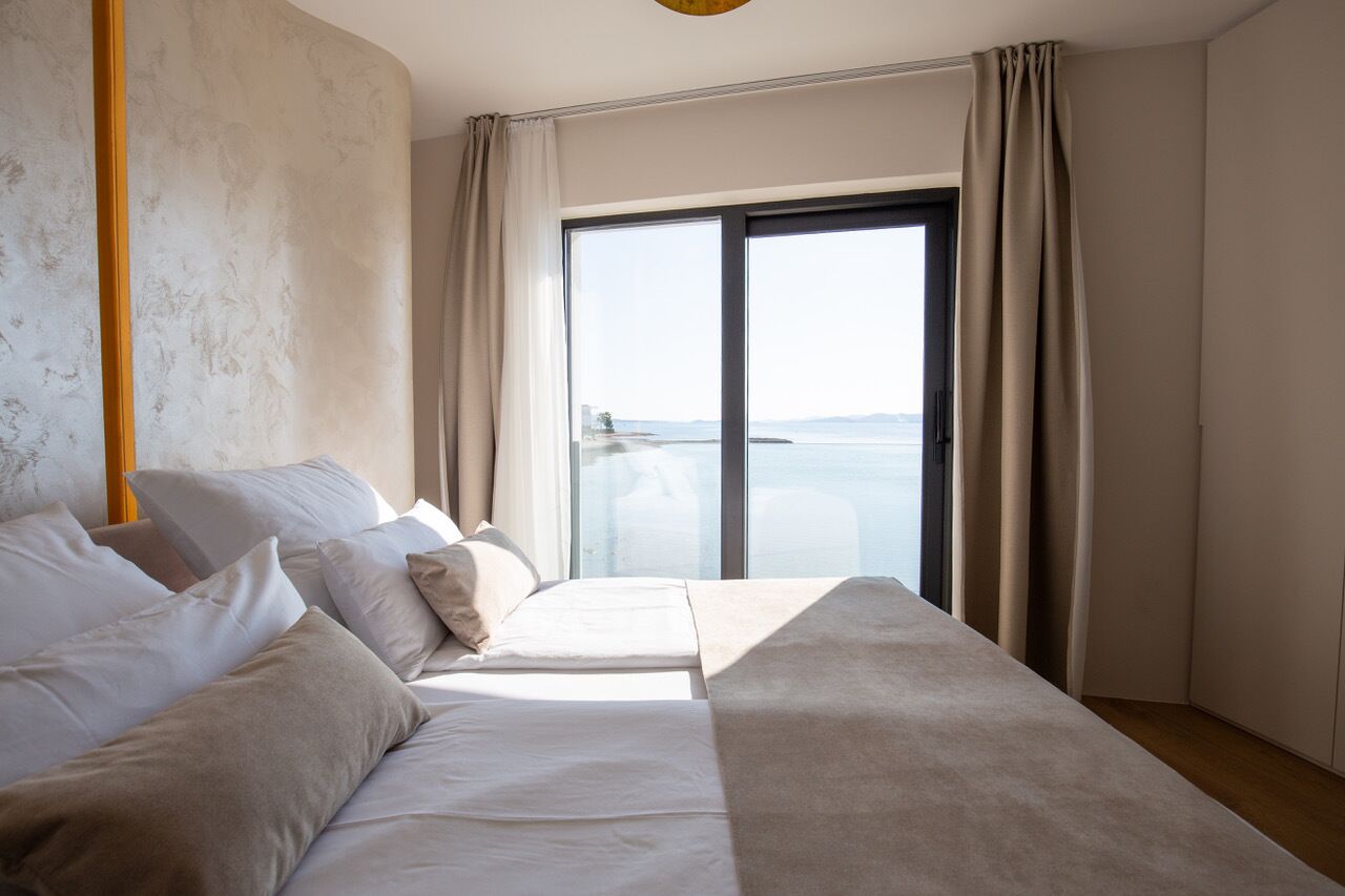 A hotel room with a bed, a large window with curtains, and a view of the sea.