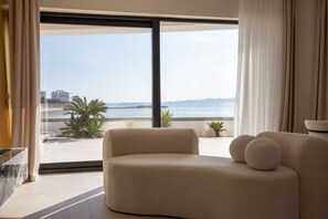 A modern living room with a large window offering a view of the sea and distant buildings. - Villa Noles (Sukošan)