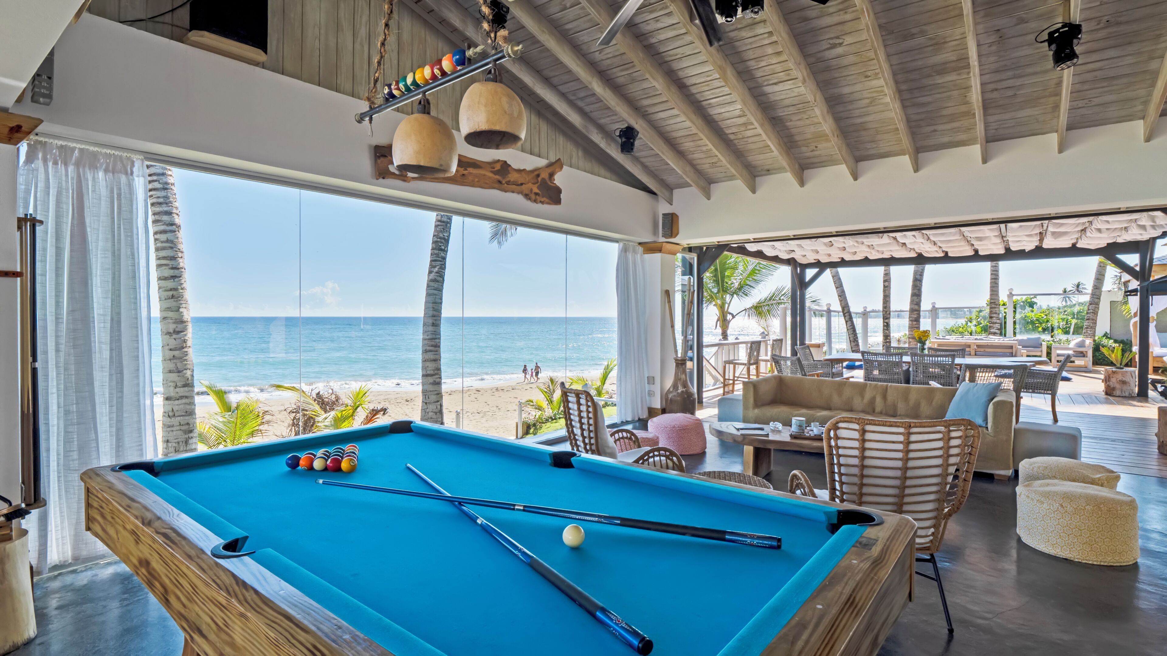 A pool table with balls, a lounge area with chairs and tables, and a view of the beach.