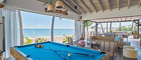 A pool table with balls, a lounge area with chairs and tables, and a view of the beach.
