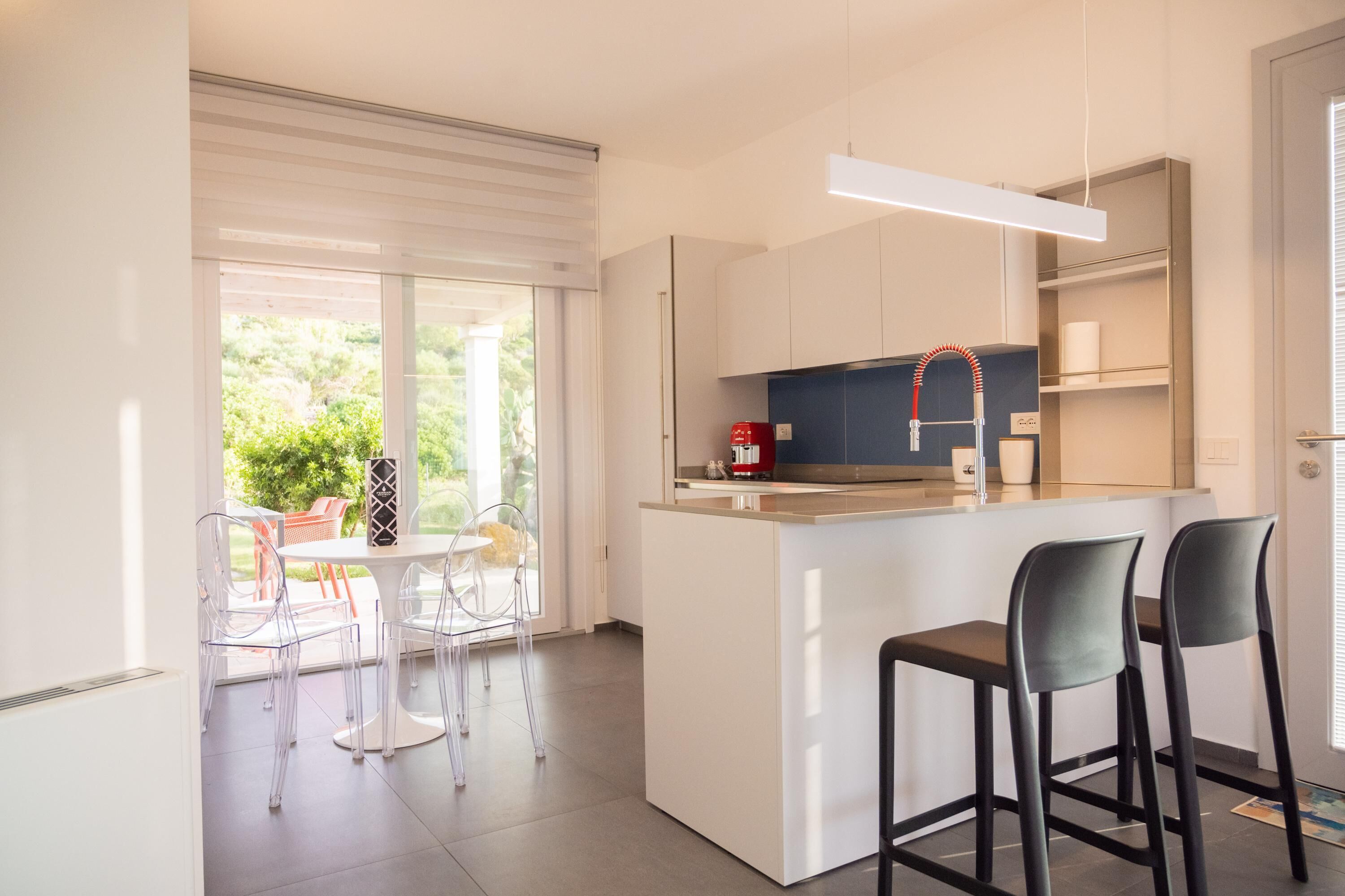 A modern kitchen with a central island, bar stools, and a dining area with transparent chairs.