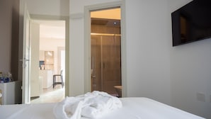 A hotel room with a bed, a TV mounted on the wall, a walk-in closet, and a bathroom visible through an open door. - Villa Fior D'acqua - Castelsardo (Castelsardo)
