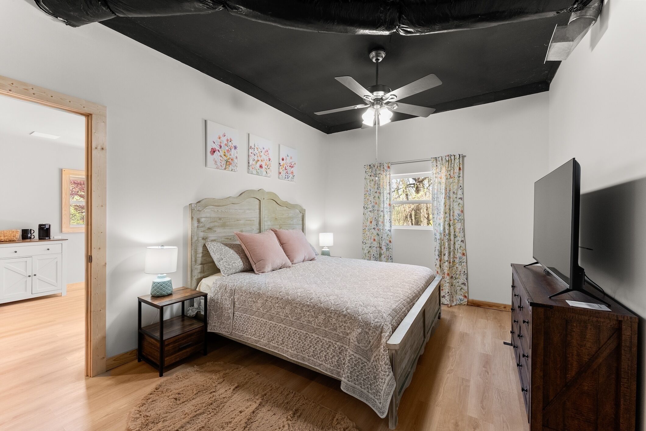 A bedroom with a bed, a TV, a ceiling fan, and a window with curtains.