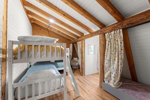 Een knus slaapkamer op zolder met houten balken, stapelbedden en een ladder.