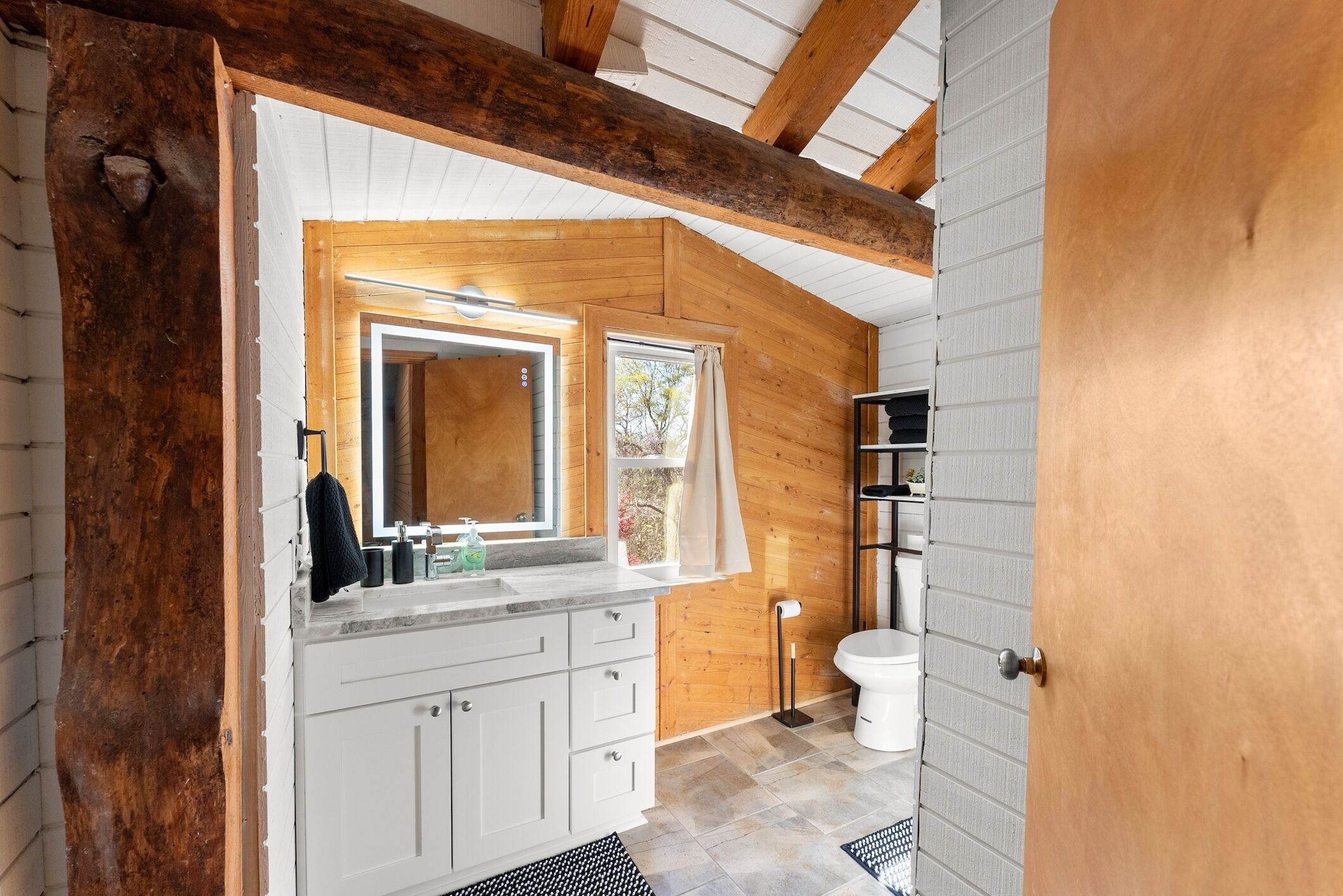 Une salle de bain moderne avec un plafond en bois, des meubles blancs, un grand miroir et des toilettes.