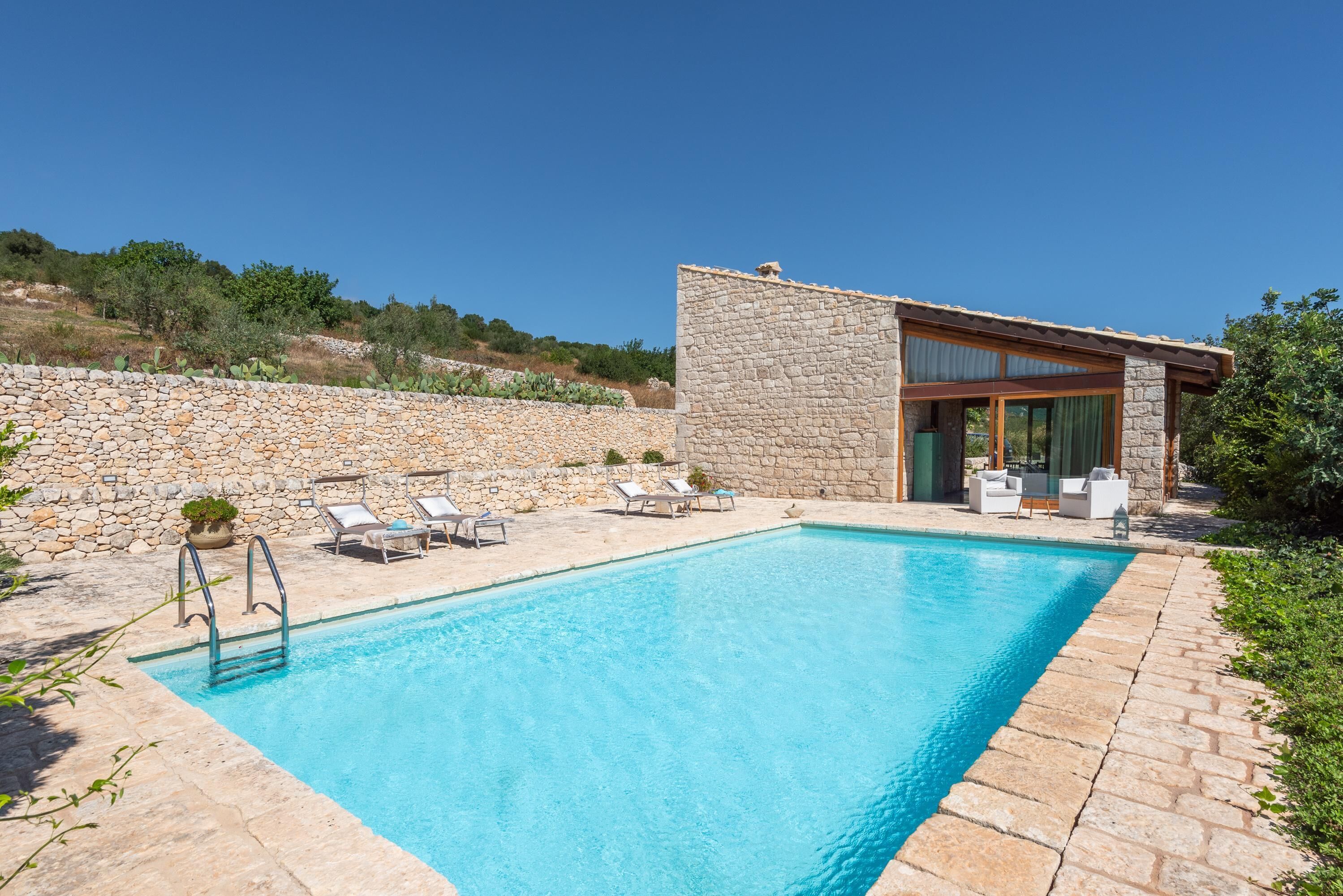 Ein moderner Poolbereich mit Steinmauern, einem klaren, blauen Pool und Liegestühlen.