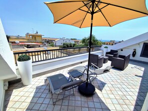 Une terrasse sur le toit, avec une table et des chaises, un grand parasol et une vue sur la mer.