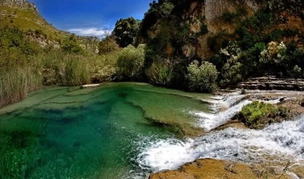 A natural landscape with a clear water body surrounded by rocky terrain and vegetation.