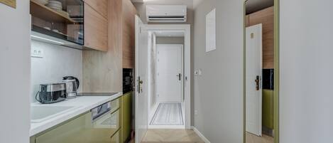 A narrow hallway with a kitchen area on one side, featuring cabinets, a coffee maker, and a microwave.