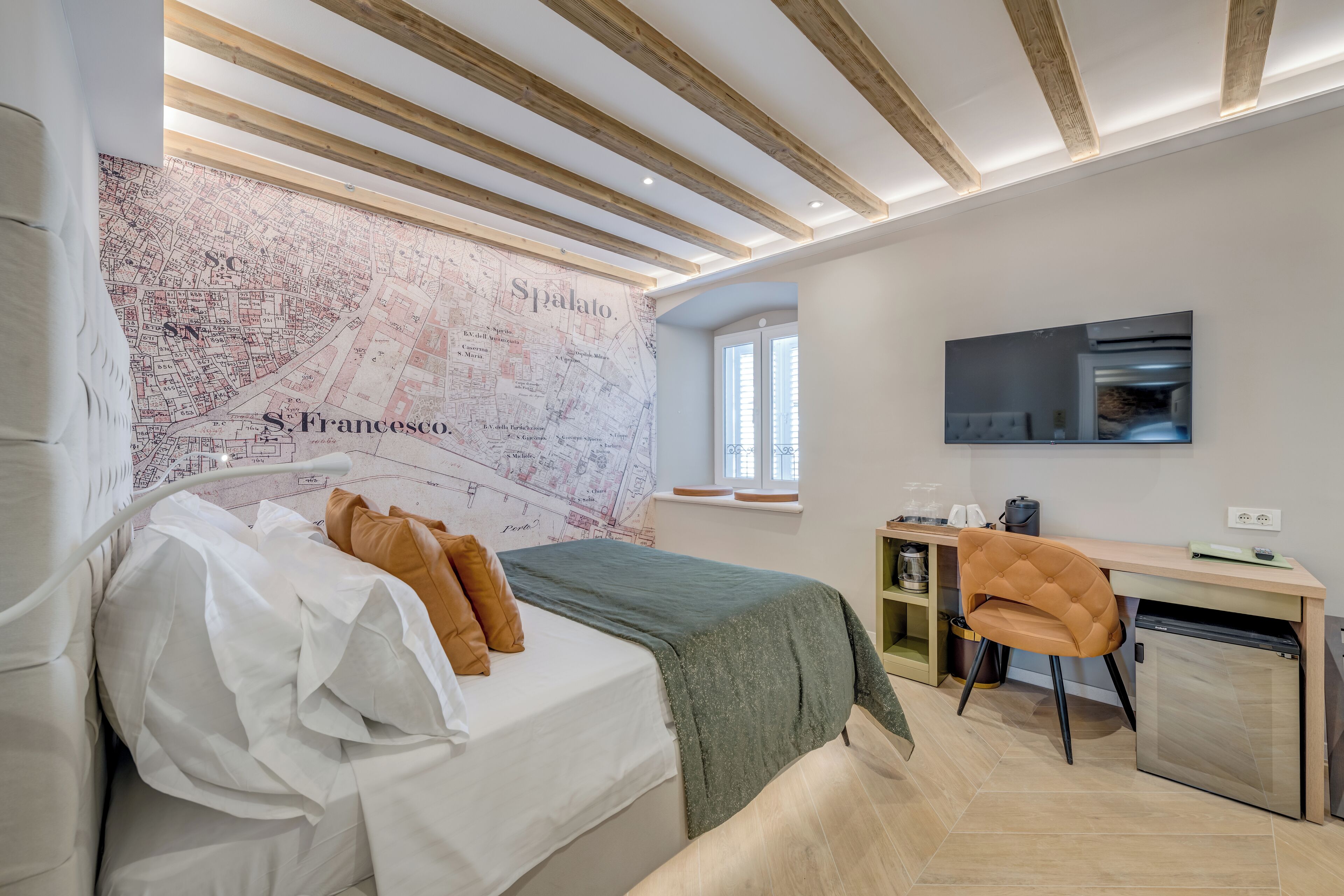 A bedroom with a bed, a desk, a chair, a television, and a map on the wall.