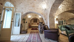 A stone-walled room with a bed, a large vase, a leather chair, and a rug.