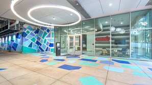 A modern building entrance with glass doors, a blue and white geometric wall design, and a tiled floor with directional arrows.