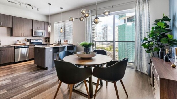 A modern kitchen with dark wood cabinets, a stainless steel dishwasher, and a dining area with a round table and black chairs.