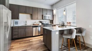 A modern kitchen with dark wood cabinets, stainless steel appliances, and a central island with bar stools.