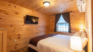 Ein Zimmer mit Holzwänden, einem Bett, einem an der Wand montierten Fernseher und einem Fenster mit Vorhängen.