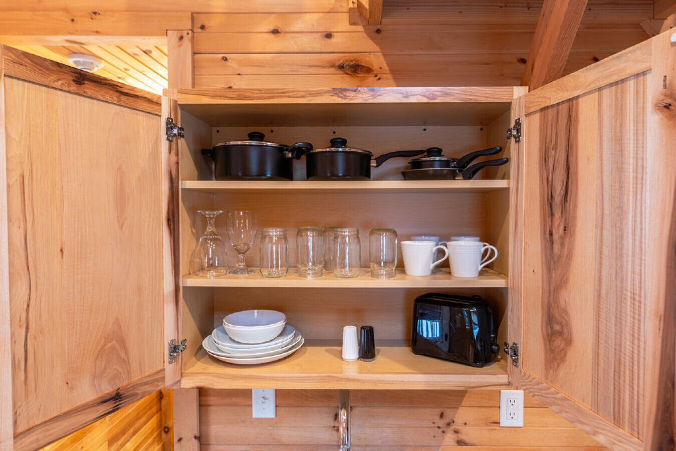 Un mueble de madera con estantes que contienen utensilios de cocina, incluyendo ollas, vasos y platos.