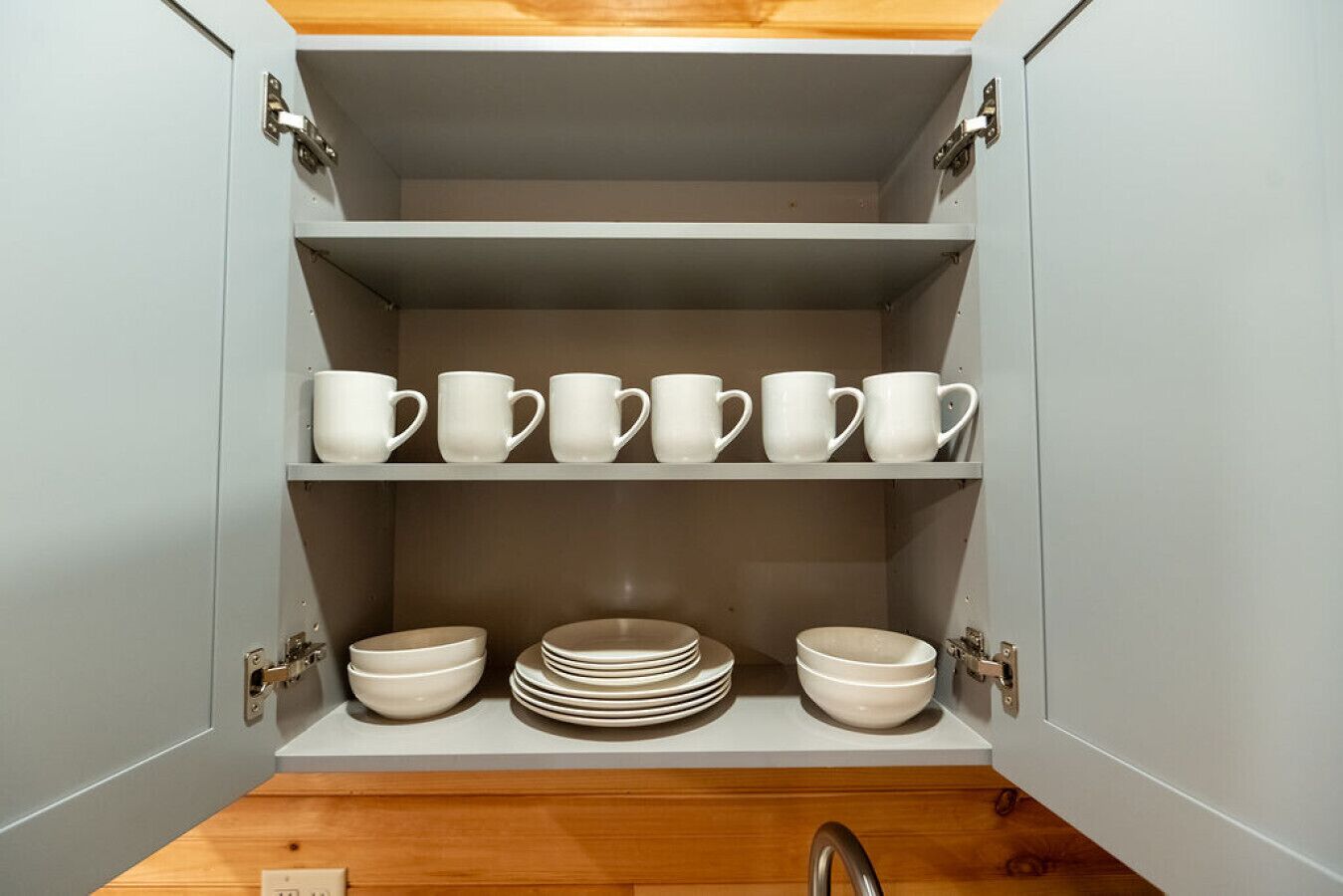 A kitchen cabinet with white mugs and bowls.