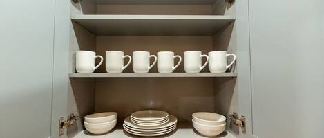A kitchen cabinet with white mugs and bowls.