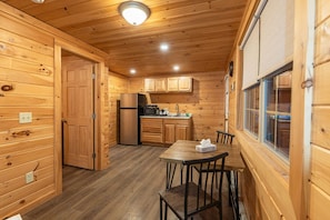 Interno di una baita in legno con cucina, zona pranzo e una finestra.