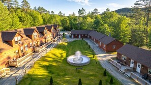 En hytte med flere bygninger, en central gårdsplads med springvand og et skovområde omkring.