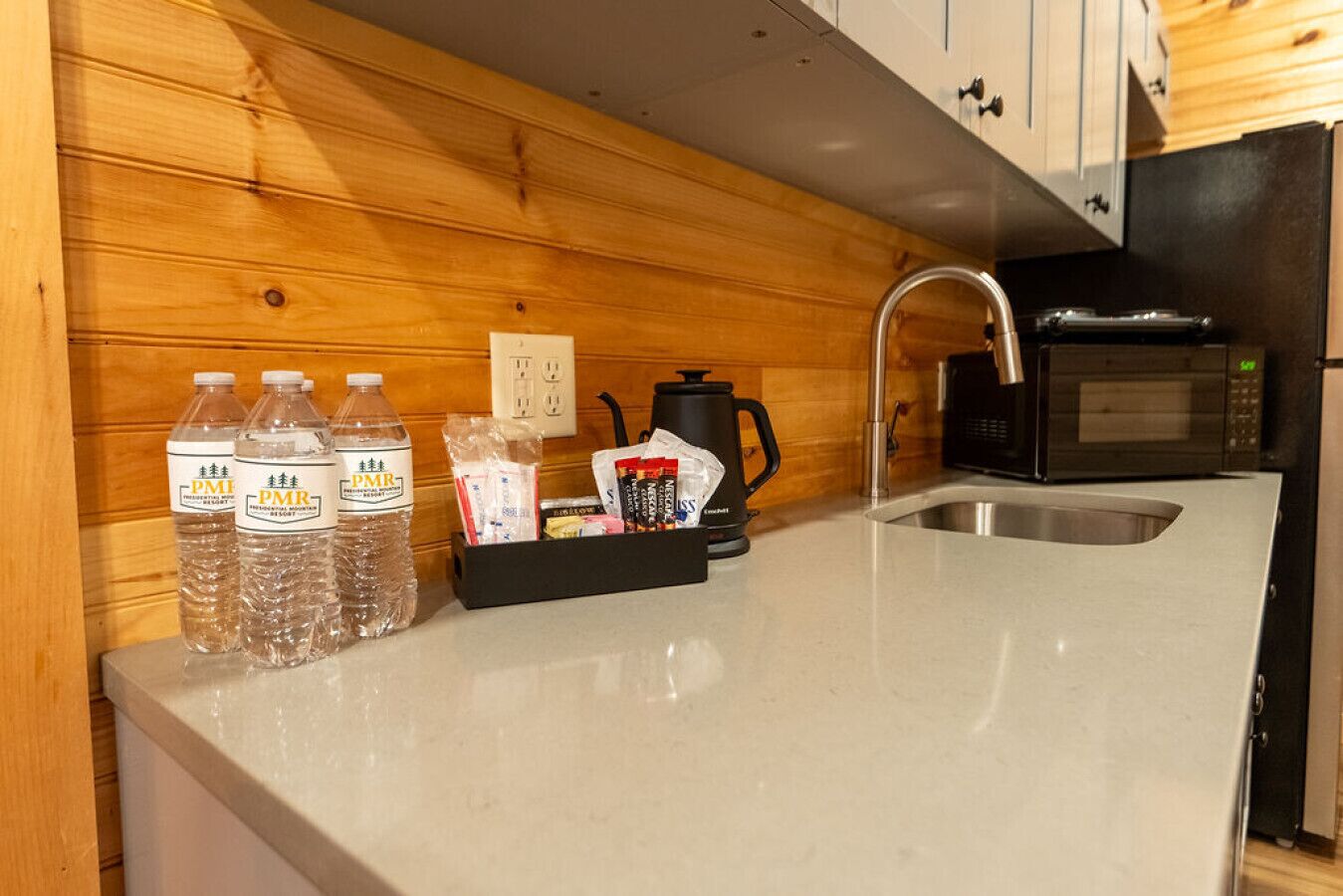 A kitchen with wooden paneling, a sink, a coffee maker, and bottled water.