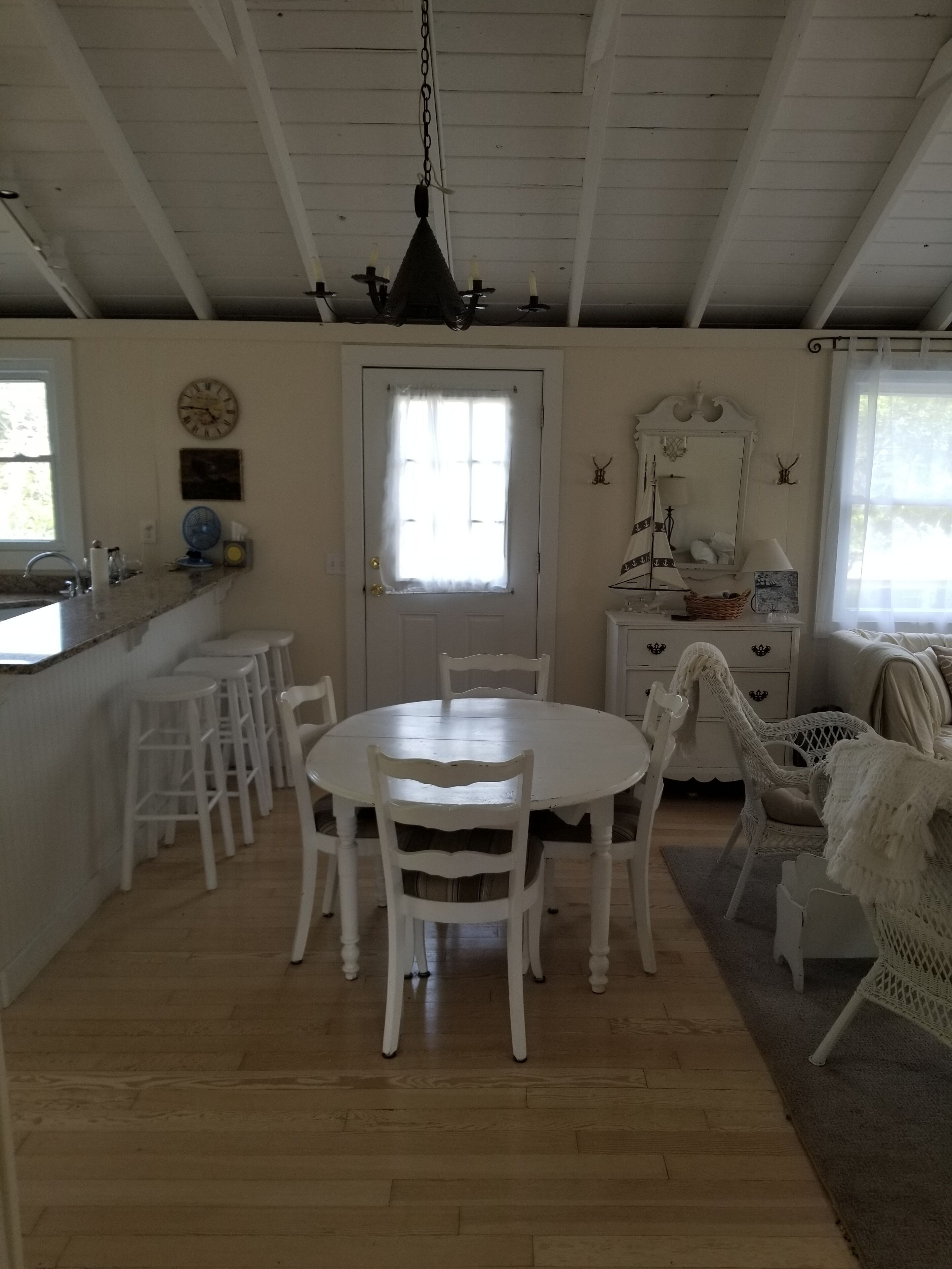Un intérieur aux couleurs claires comprenant une table à manger, des chaises, un coin cuisine et un espace de vie avec un canapé et un fauteuil.