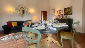A dining area with a round table set for four, surrounded by green chairs. A black sofa with red and yellow cushions is against the wall.