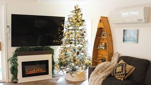 Ein Wohnzimmer mit Kamin, Weihnachtsbaum, Flachbildfernseher und einer Couch.