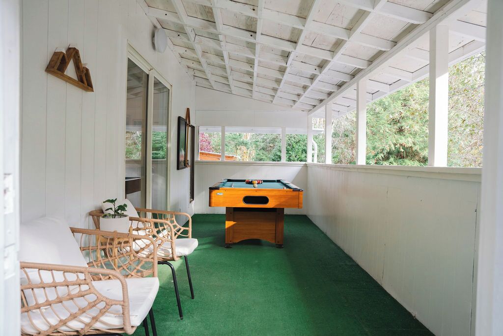 Een kamer met een pooltafel, rieten stoelen en uitzicht door grote ramen.