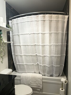 A bathroom with a white shower curtain, a white toilet, and a black sink. - Welcome to Falcon Escape (Calgary)