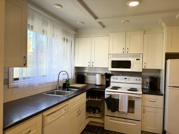 A kitchen with white cabinets, a stainless steel sink, a microwave, an oven, and a dishwasher. - Welcome to Falcon Escape (Calgary)